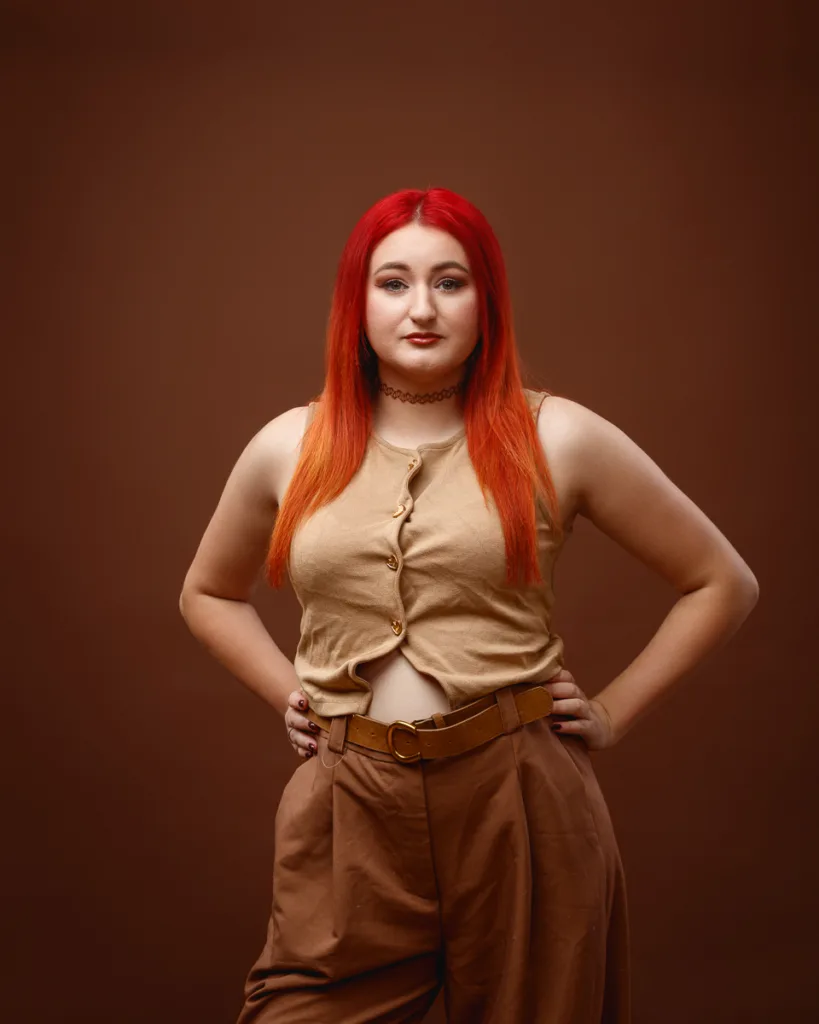 Person with red hair wearing brown outfit posing confidently