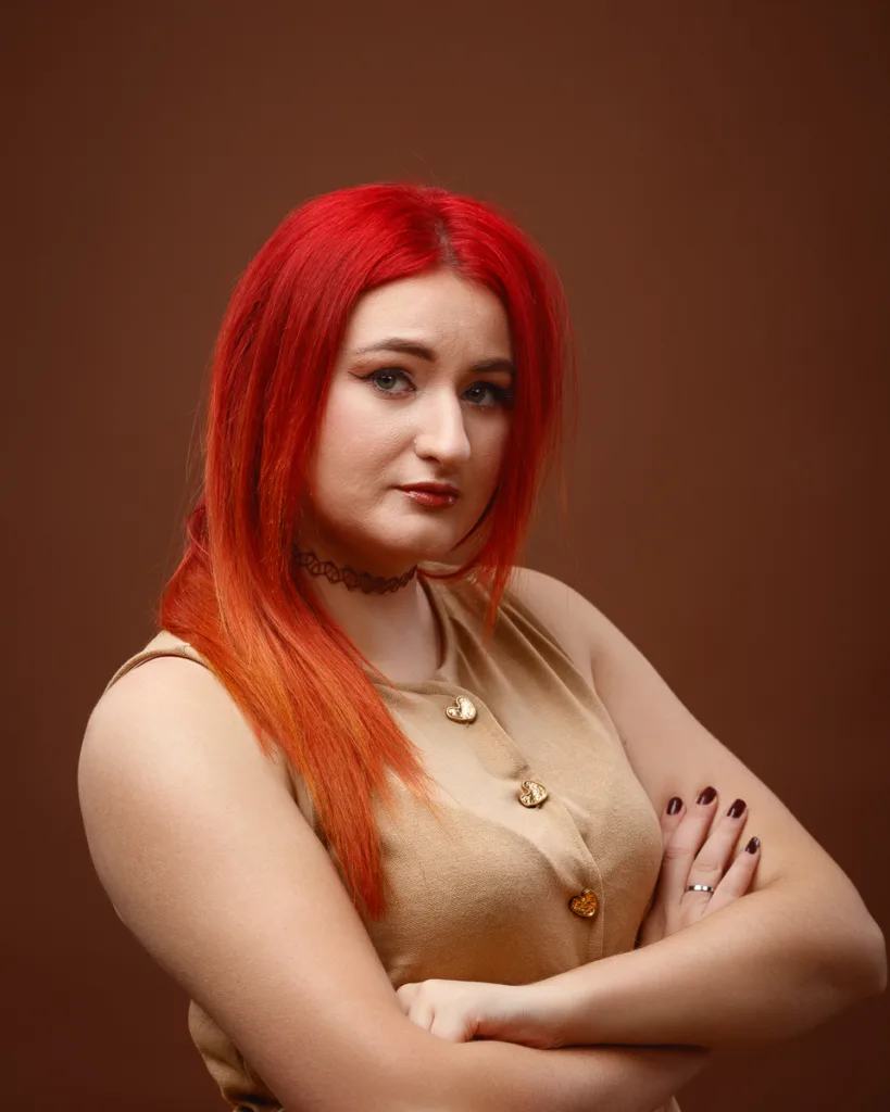 Person with red hair posing confidently against brown background