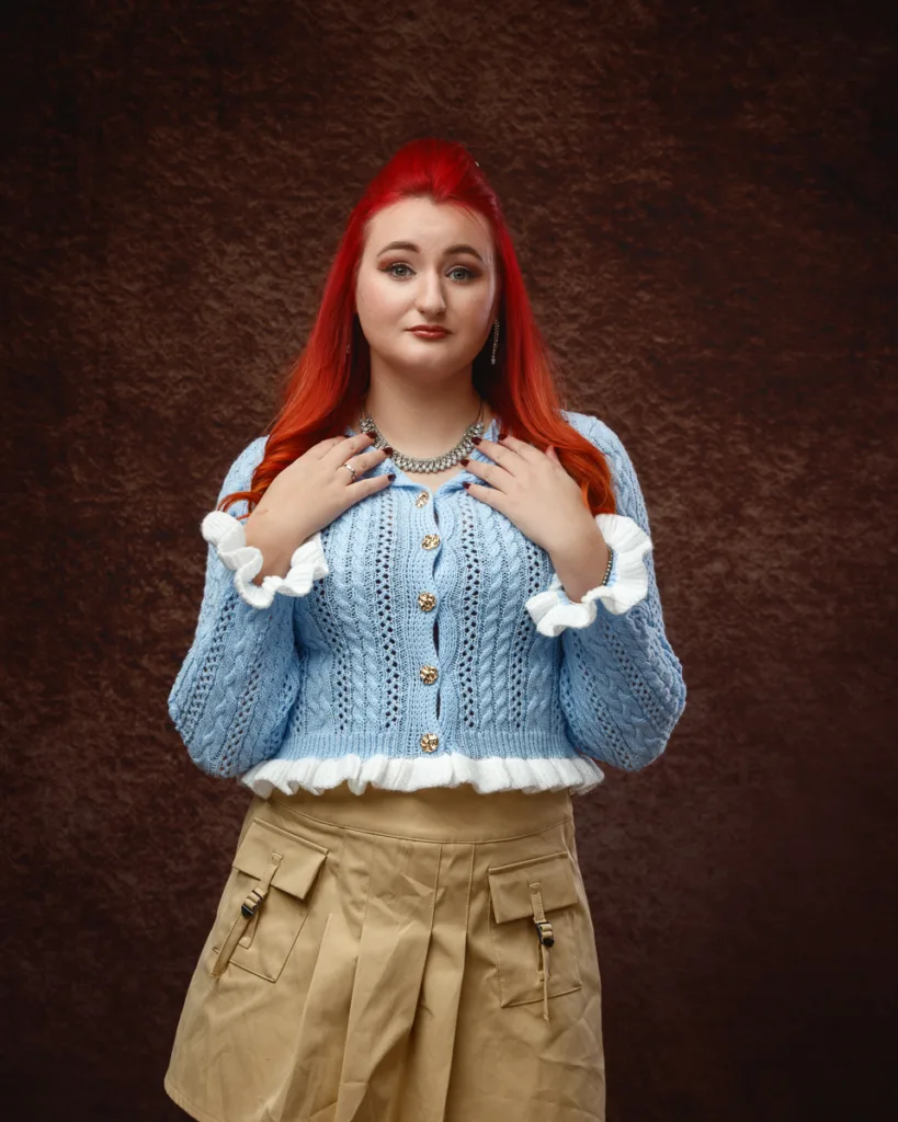 Person with red hair wearing blue jumper and beige skirt