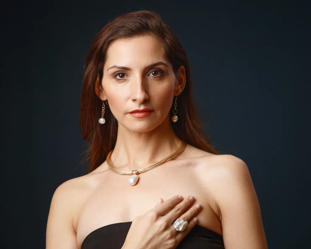 Woman wearing pearl jewellery against dark backdrop.