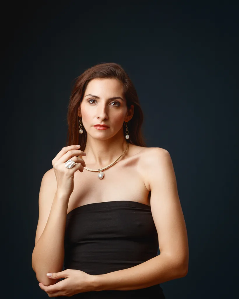 Woman in black dress with pearl jewellery.