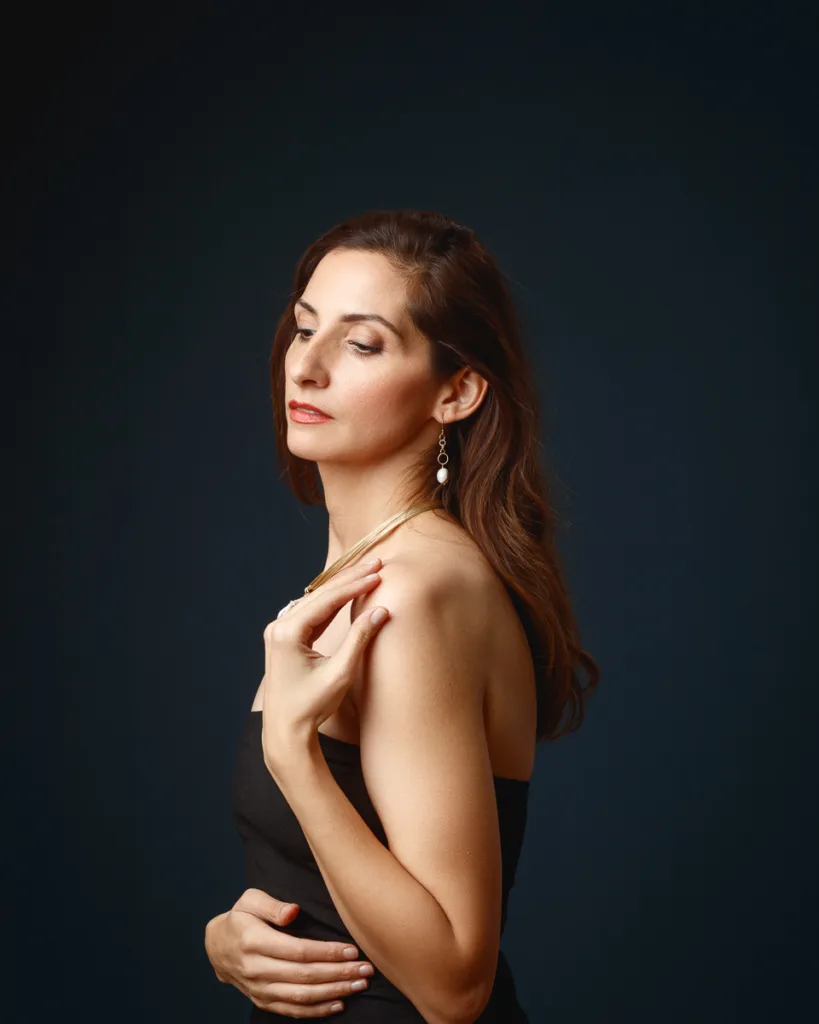 Woman wearing black dress, elegant pose, dark background.