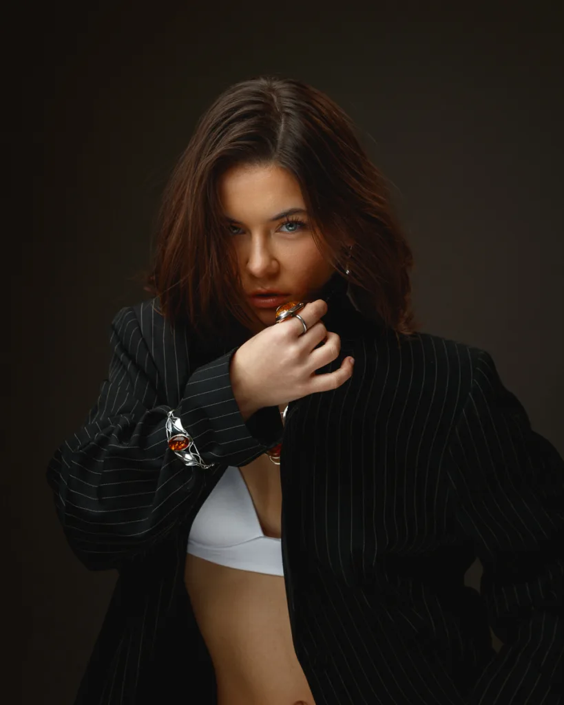 Woman in pinstripe jacket, white top, dark background.