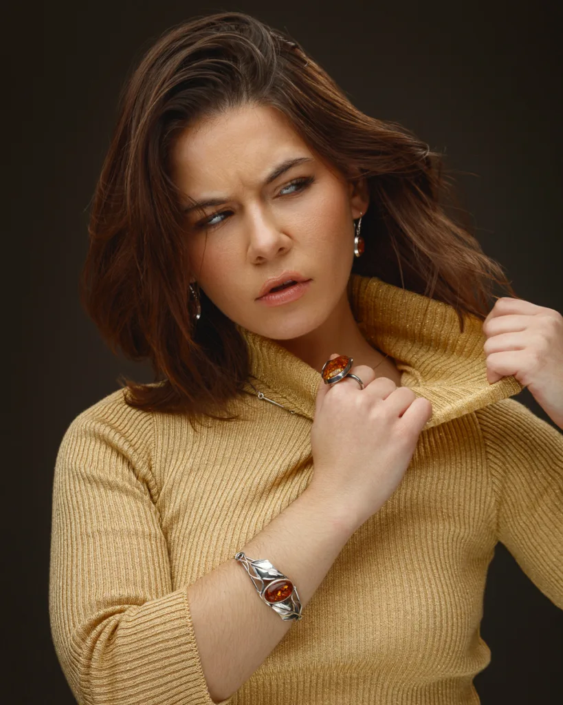 Woman with jewellery wearing beige sweater, looking pensive.