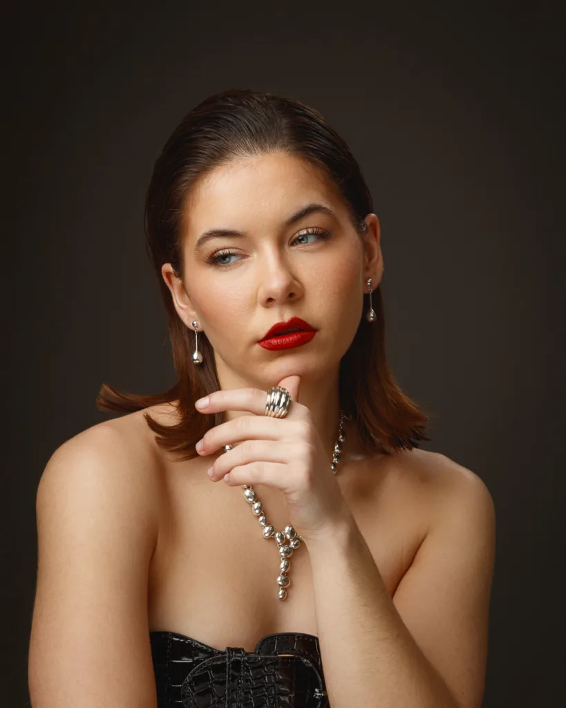 Person wearing elegant jewellery, red lips, thoughtful pose.