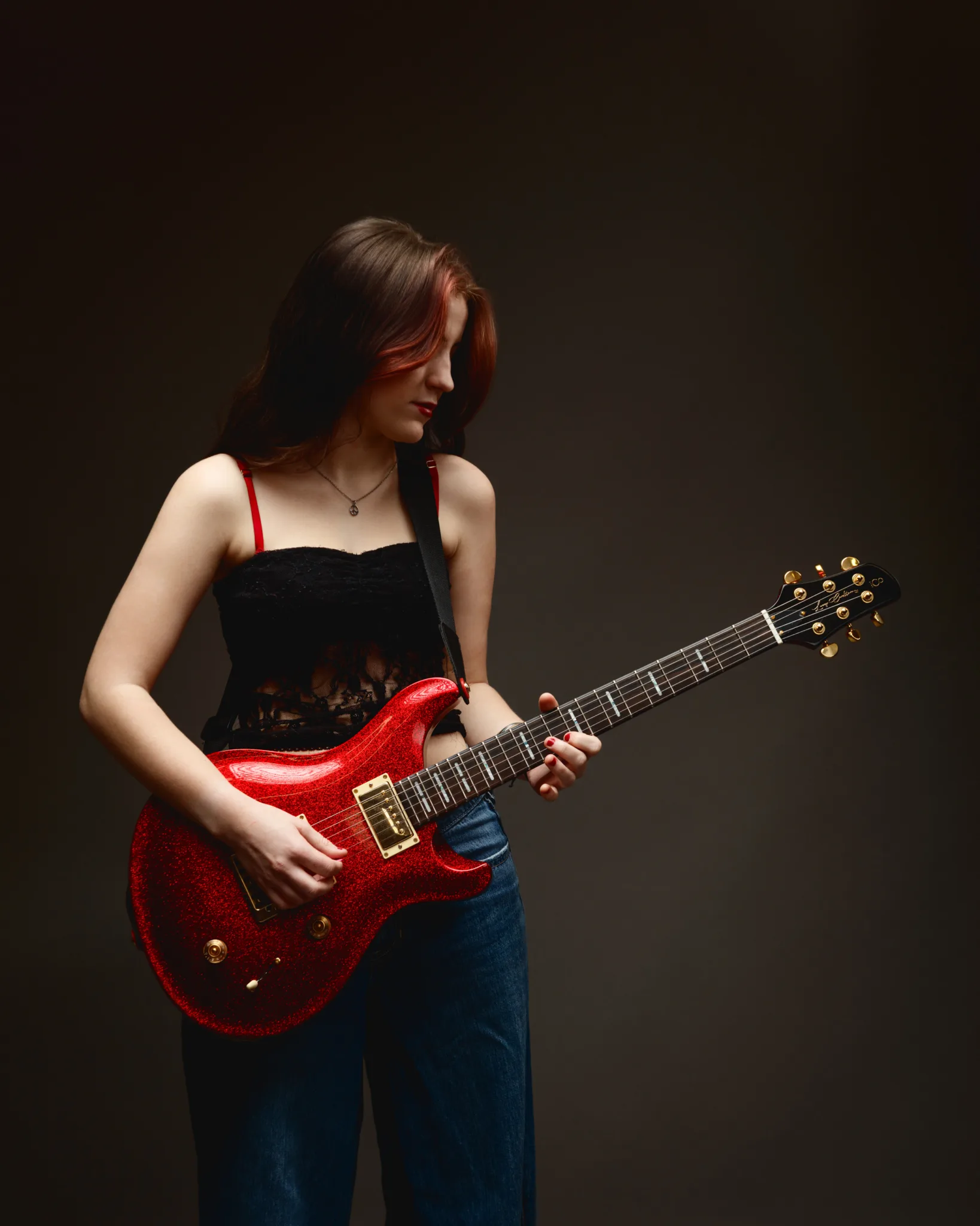 Woman playing red electric guitar in studio.