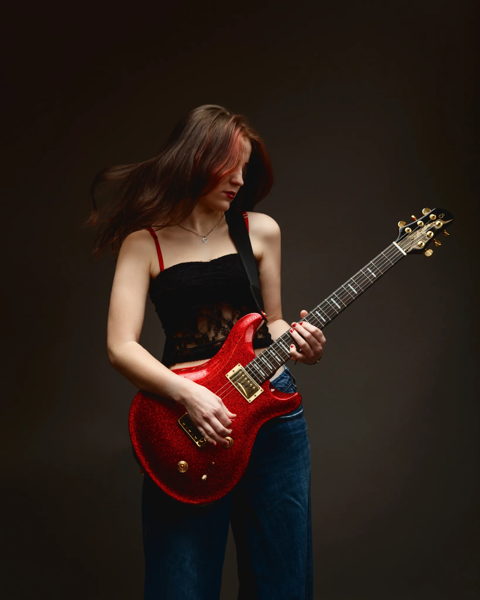 Woman playing red electric guitar passionately.