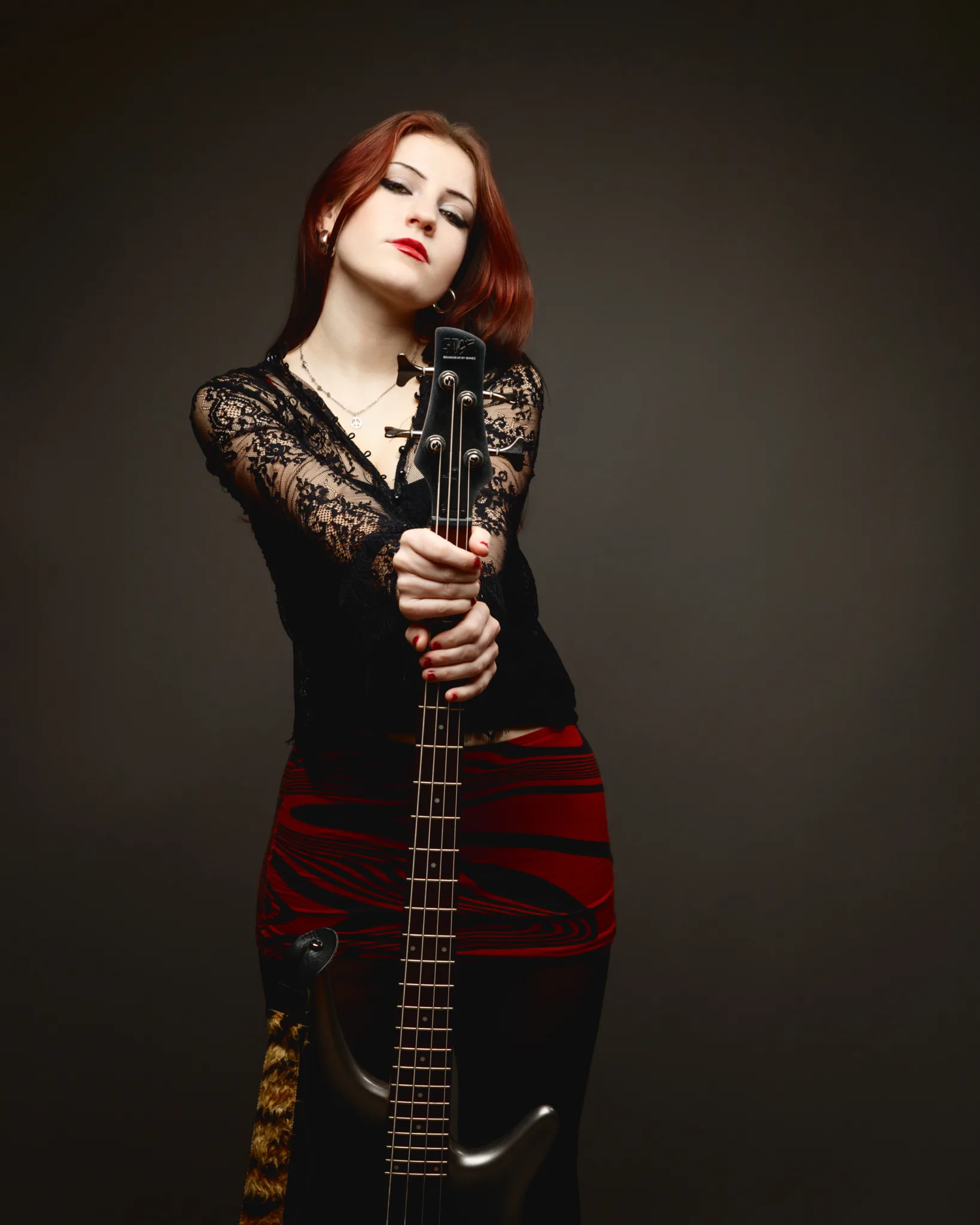 Woman holding bass guitar against dark background.