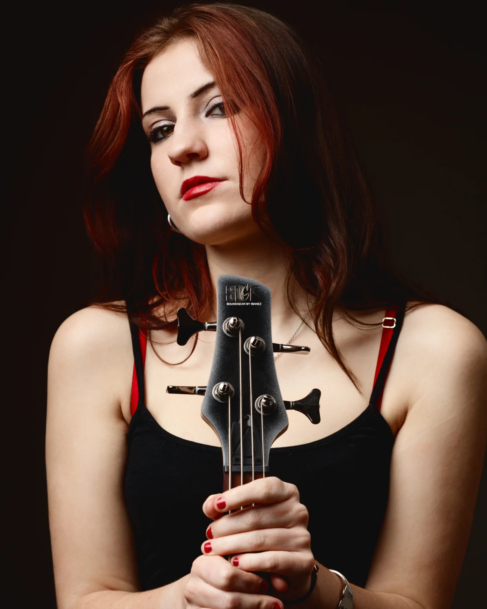 Woman holding bass guitar, black tank top, red lipstick.