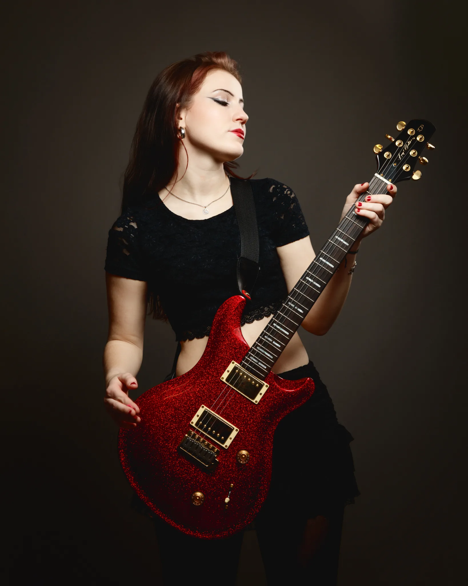 Woman playing red electric guitar on dark background.