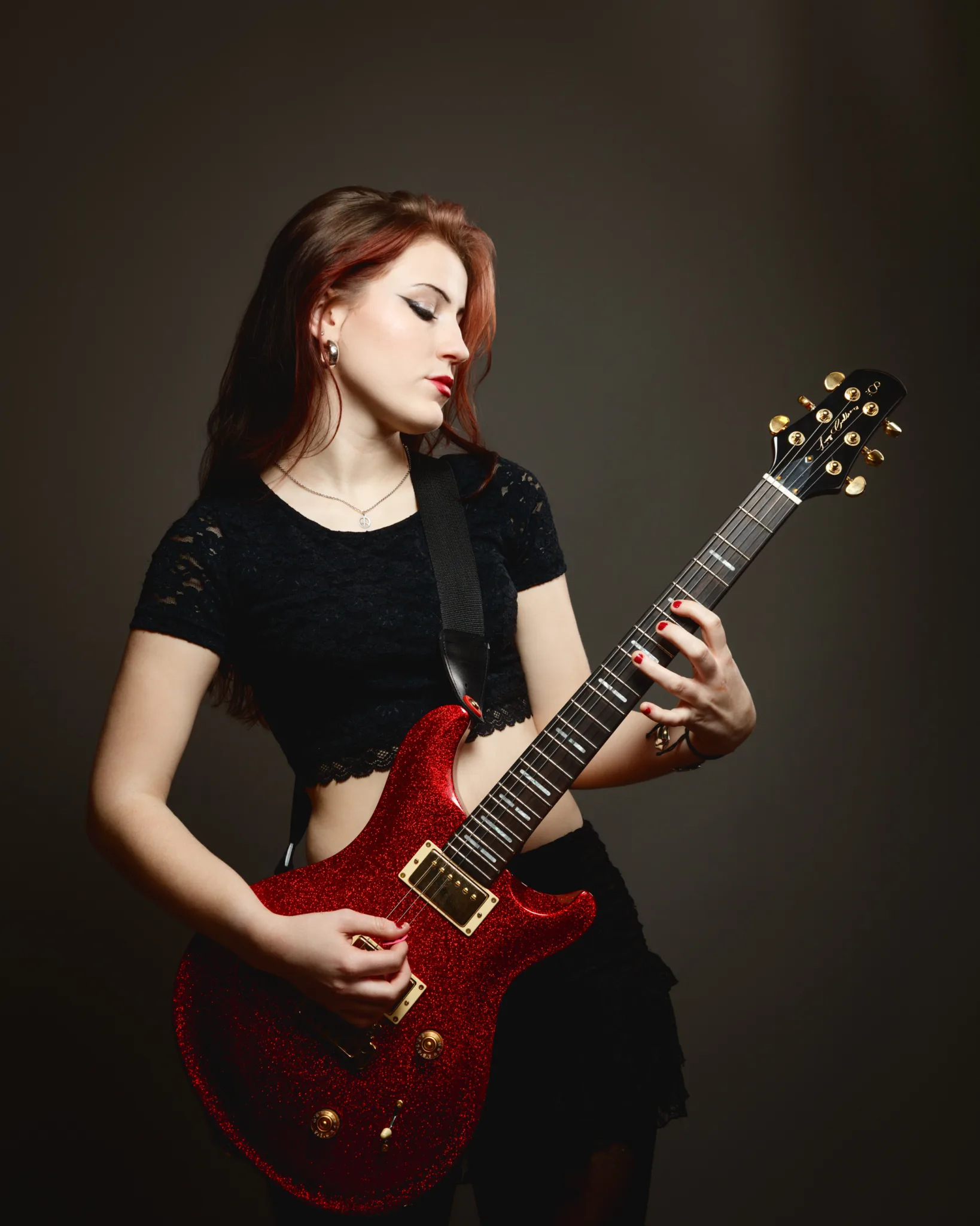 Woman playing electric guitar on dark background.