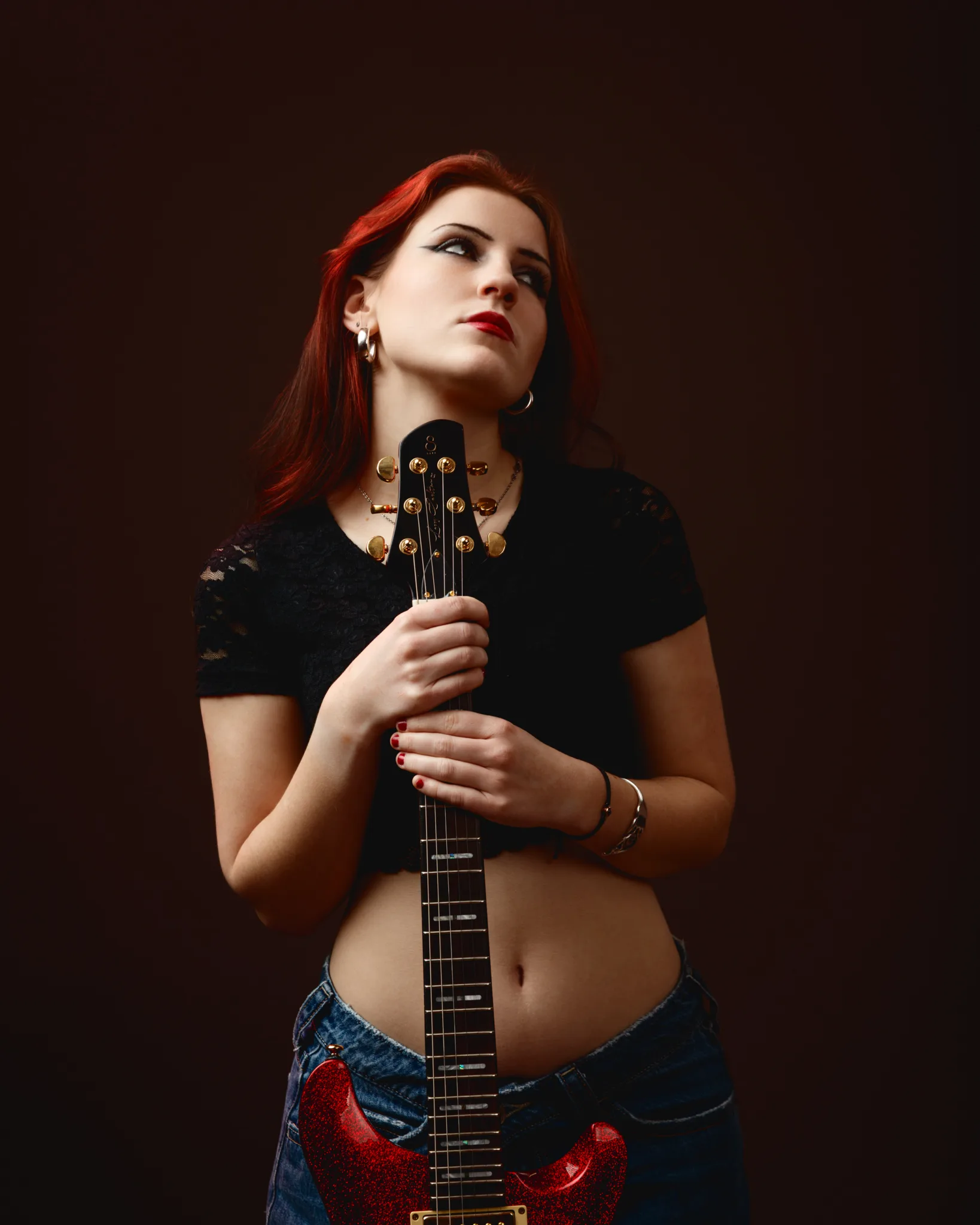 Young woman holding electric guitar, looking upward.