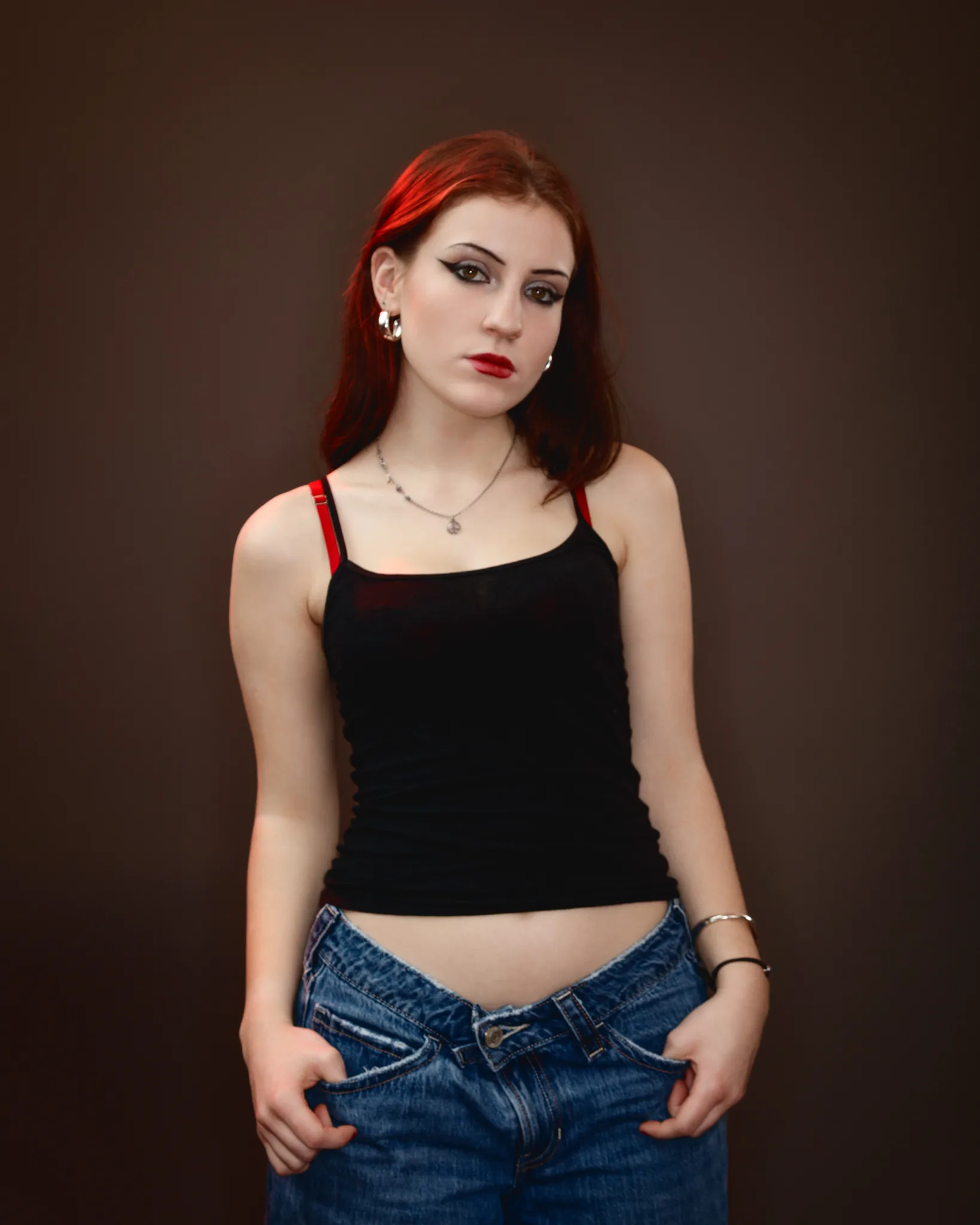 Woman in black top and jeans posing against brown background.