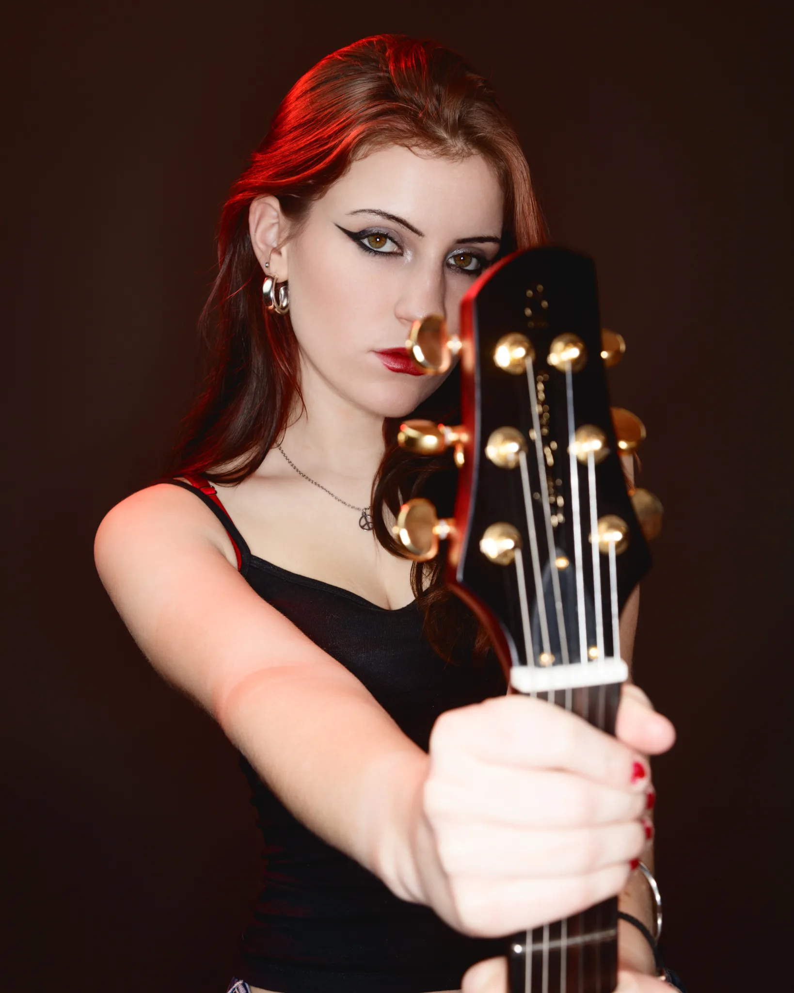 Woman holding guitar, intense expression, red lighting.